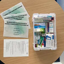 Plastikkiste mit unterschiedlichen Medikamentenverpackungen, Aktionskarten und Anleitung