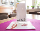 Tisch mit pinkfarbener Tischdecke. Darauf Speisekarte mit der Aufschrift ASB und CAfé LIS  in Plexiglasständer.