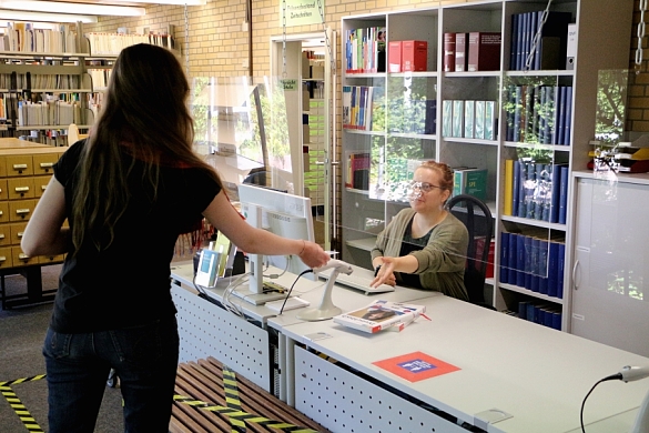 Ausleihtresen mit Mitarbeiterin, die einen Bibliotheksausweis zum Verbuchen entgegennimmt