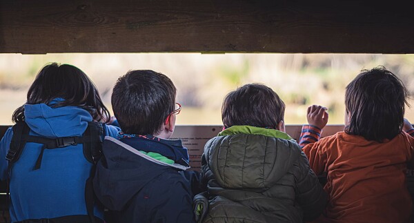 Mehrere Kinder schauen durch einen Spalt einer Hütte nach draußen 