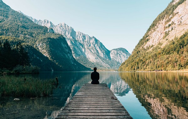 Symbolbild: ein Mensch sitzt auf einem Steg und blickt auf einen See