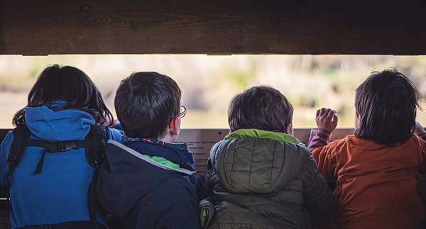 Mehrere Kinder schauen durch einen Spalt einer Hütte nach draußen 