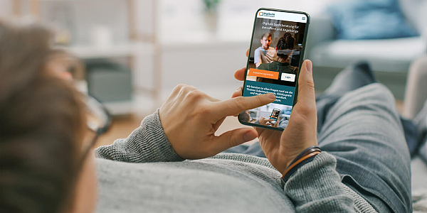 Foto: Hände halten ein Smartphone, auf dem die Hilfsseiten von DigiSucht zu sehen sind. Mit Schriftzügen