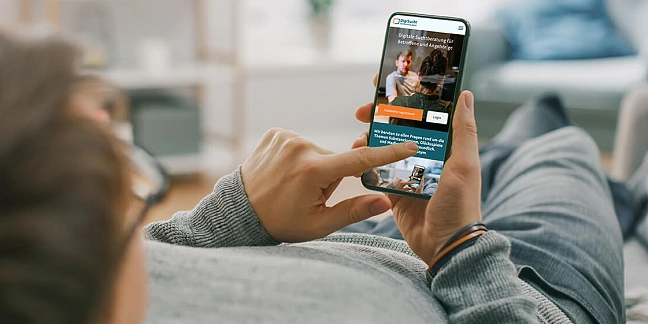 Foto: Hände halten ein Smartphone, auf dem die Hilfsseiten von DigiSucht zu sehen sind. Mit Schriftzügen