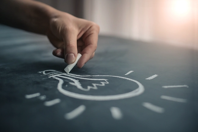 Hand zeichnet mit Kreide eine Glühbirne auf eine Tafel