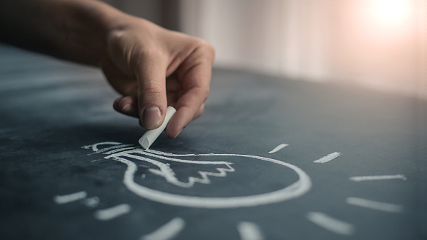 Hand zeichnet mit Kreide eine Glühbirne auf eine Tafel