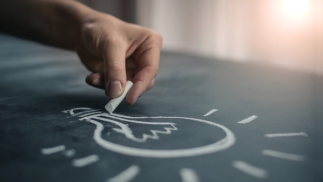 Hand zeichnet mit Kreide eine Glühbirne auf eine Tafel