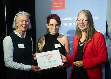 Drei Personen bei der Übergabe einer Plakette. 