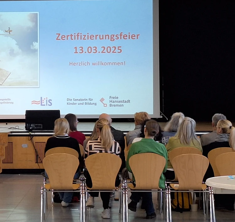 Ein Bild von der Zertifizierungsfeier, bei der man sitzende Personen und die Bühne sieht