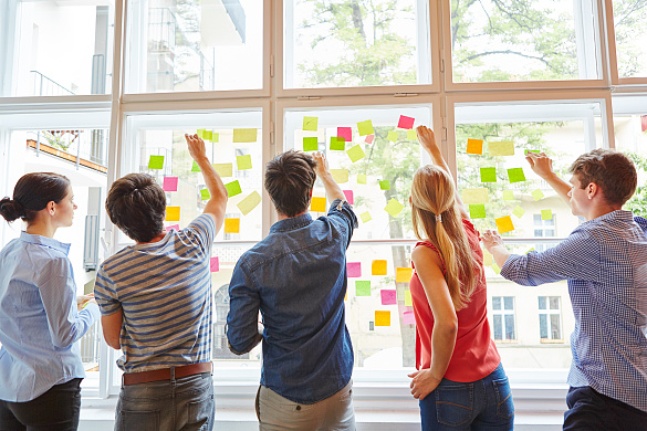 Junge Leute nutzen Fensterfront zur Ideensammlung mit Post-Its