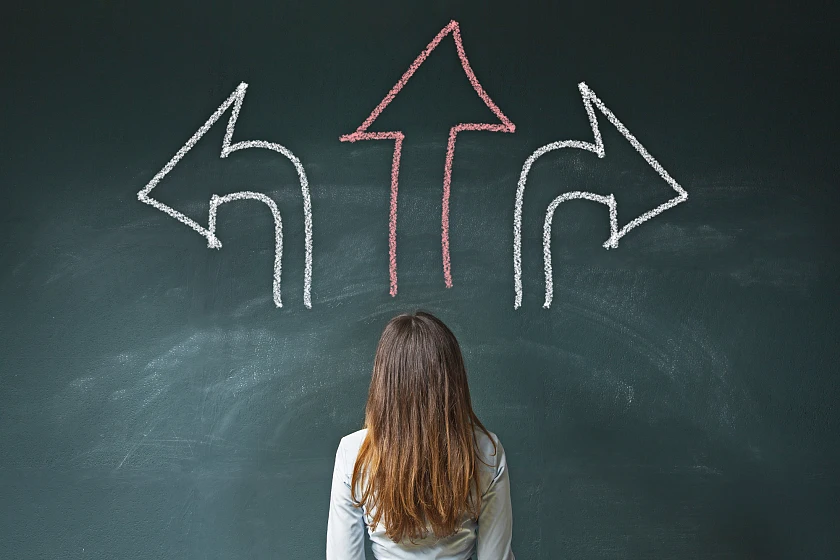 Person in Rückenansicht vor Tafel, auf der mit Kreide gezeichnete Pfeile nach rechts, links und oben sind 