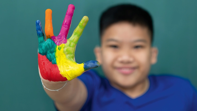 Junge mit bunt bemalten Händen und der Aufschrift Inklusives Wissen: Angebote online buchen