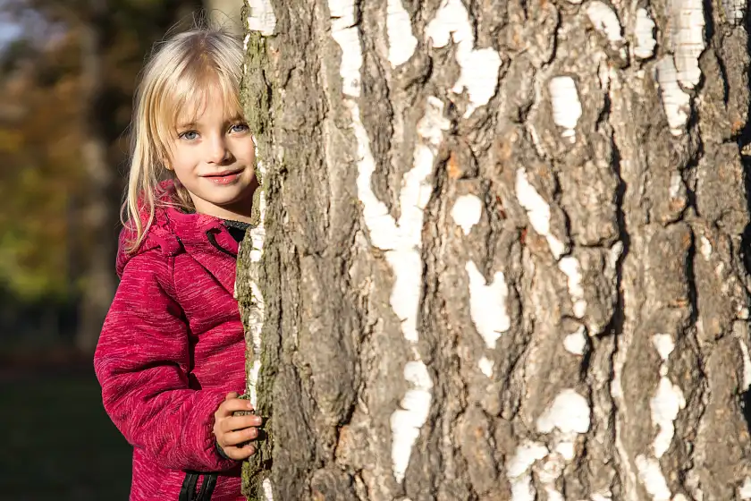 Mädchen versteckt sich hinter Baum